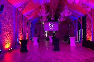 Salle de réception avec éclairage coloré, tables hautes et écran de projection au fond.
