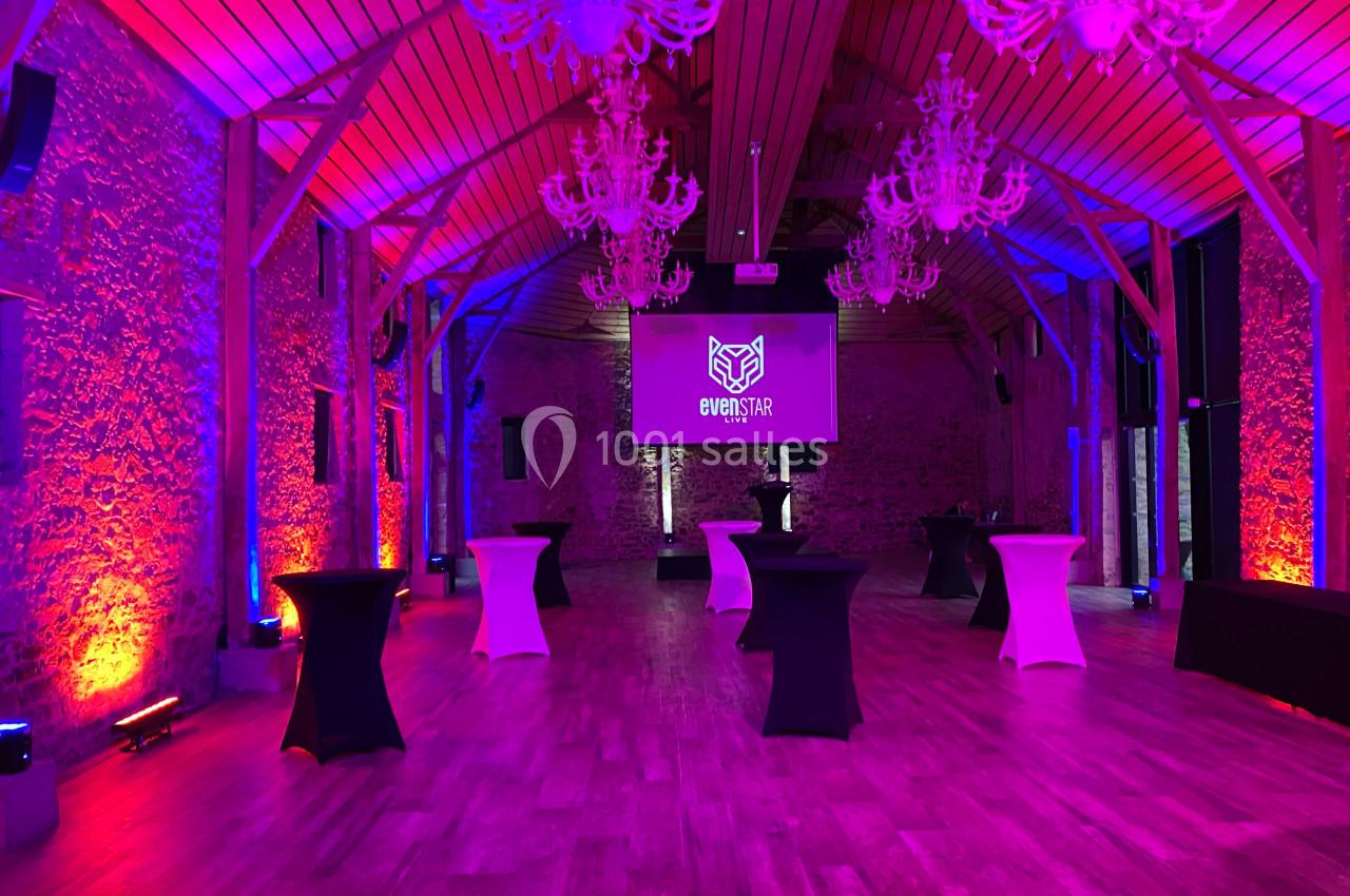 Salle de réception avec éclairage coloré, tables hautes et écran de projection au fond.