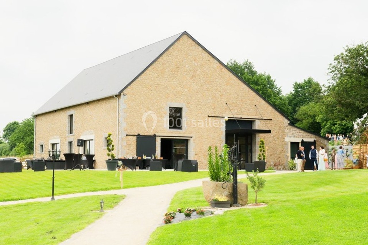 Bâtiment en pierre avec toit en ardoise, entouré de pelouses et d'arbres, avec des personnes à l'extérieur.