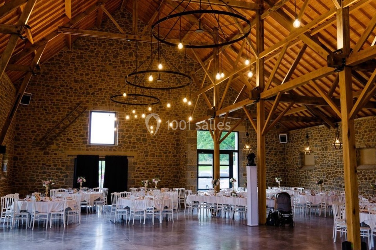 Salle de réception en pierre avec poutres apparentes, tables dressées et éclairage suspendu.