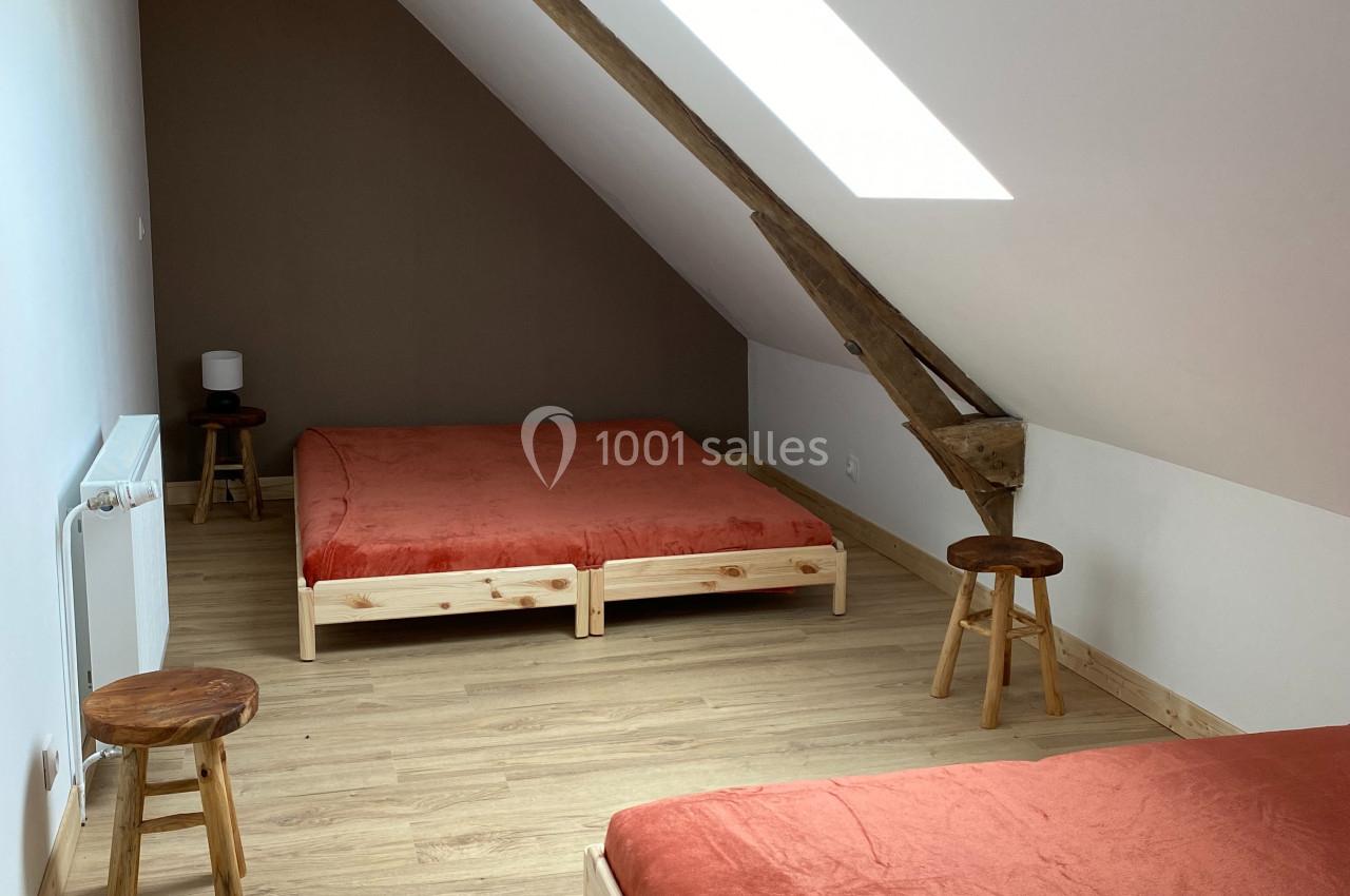 Deux lits avec draps orange dans une chambre mansardée lumineuse, parquet en bois clair et poutre apparente.