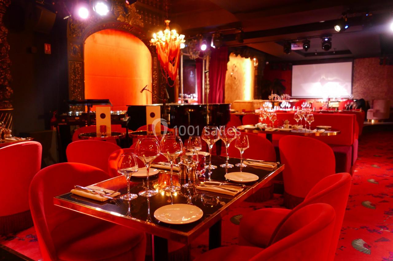 Salle de restaurant élégante avec tables dressées, chaises rouges, éclairage tamisé et décorations raffinées.