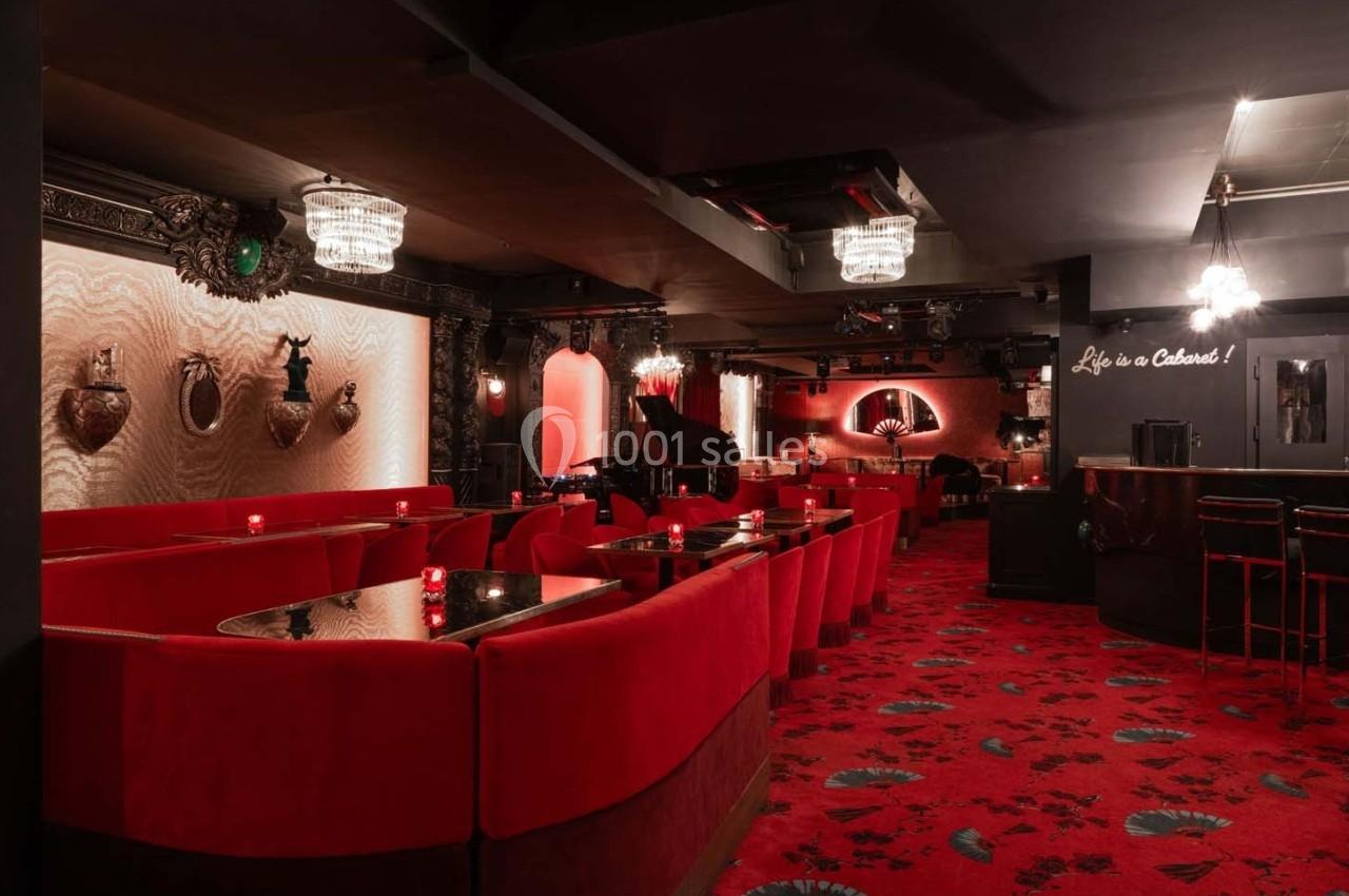 Salle de cabaret élégante avec banquettes rouges, lustres en cristal, piano et décorations murales sophistiquées.