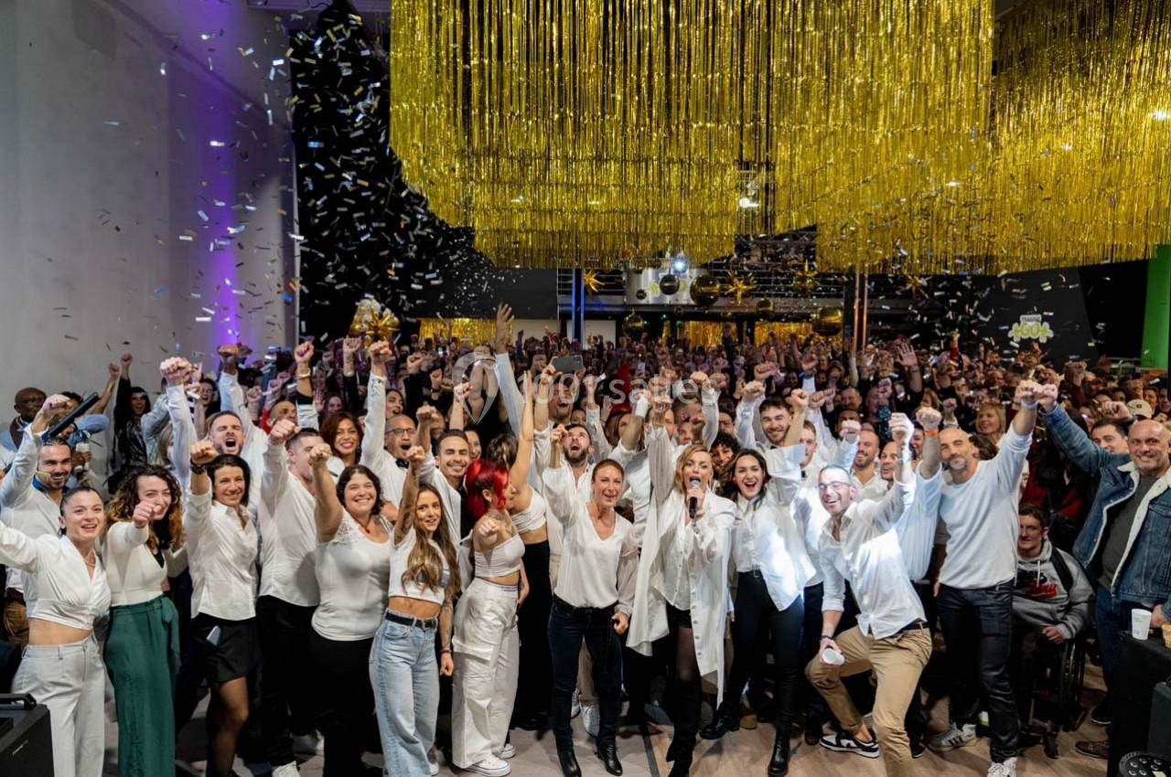 Groupe de personnes souriantes célébrant sous des guirlandes dorées et des confettis dans une salle festive.