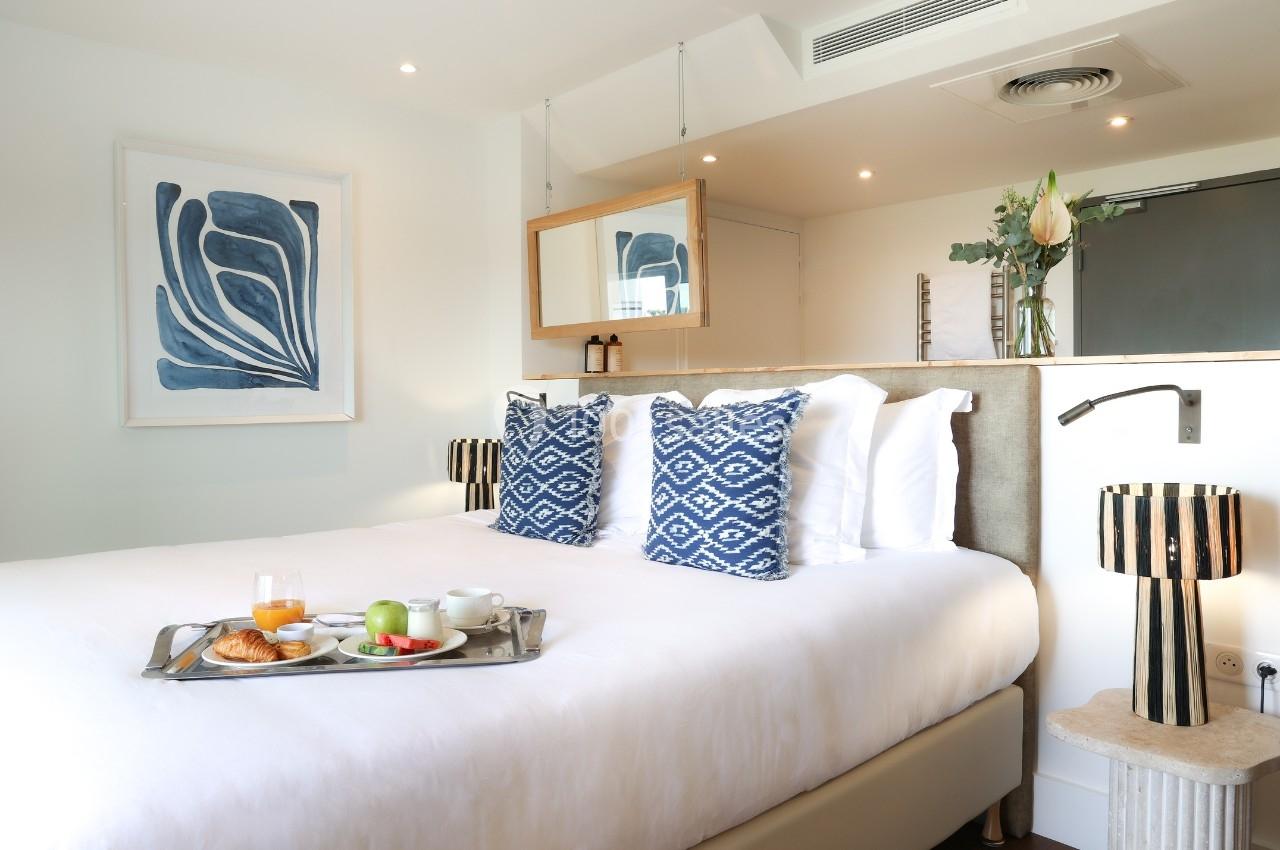 Chambre lumineuse avec lit double, coussins à motifs bleus, plateau petit-déjeuner et décoration moderne.