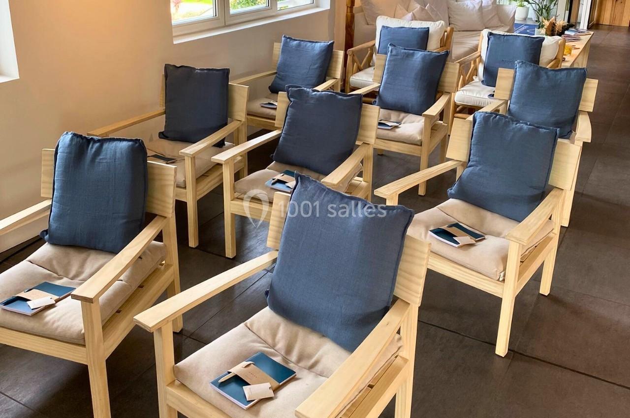 Chaises en bois clair avec coussins bleus alignées dans une salle, chaque siège portant un carnet et un stylo.