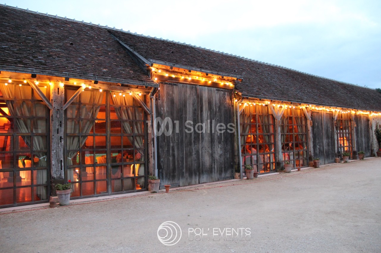 Grange en bois avec grandes baies vitrées éclairées par des guirlandes lumineuses, en soirée.