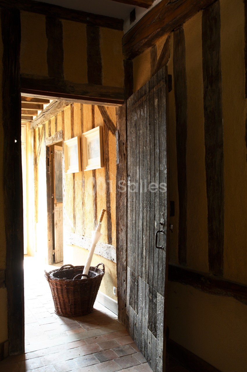 Porte en bois ouverte sur un couloir lumineux avec murs en colombages, panier en osier posé au sol.