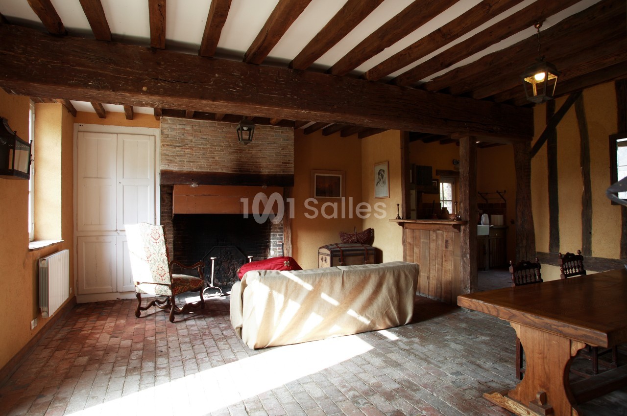 Salon rustique avec poutres apparentes, cheminée en briques, mobilier ancien et sol en carreaux de terre cuite.