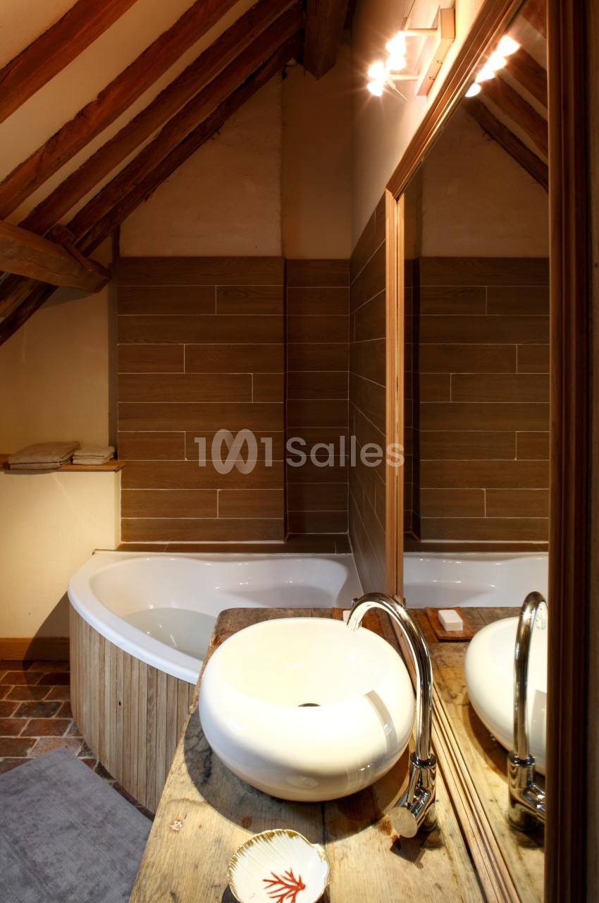 Salle de bain avec baignoire d'angle, vasque ronde sur plan en bois, miroir et murs en carrelage effet bois.