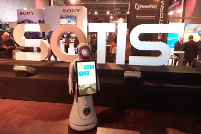 Robot humanoïde blanc équipé d'un écran et d'un plateau, présenté dans un environnement intérieur avec plantes et…