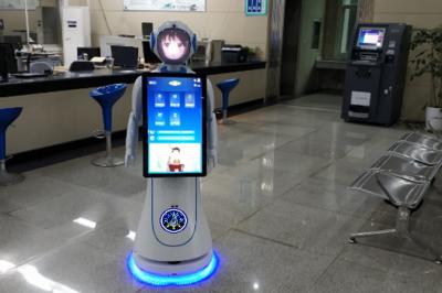 Robot humanoïde blanc équipé d'un écran et d'un plateau, présenté dans un environnement intérieur avec plantes et…