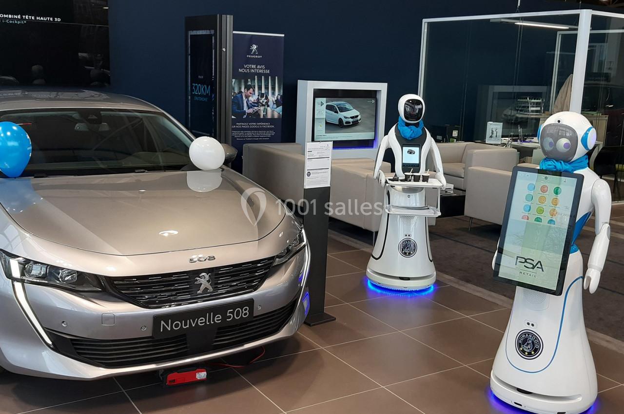 Deux robots interactifs à côté d'une voiture Peugeot 508 exposée dans un showroom automobile.