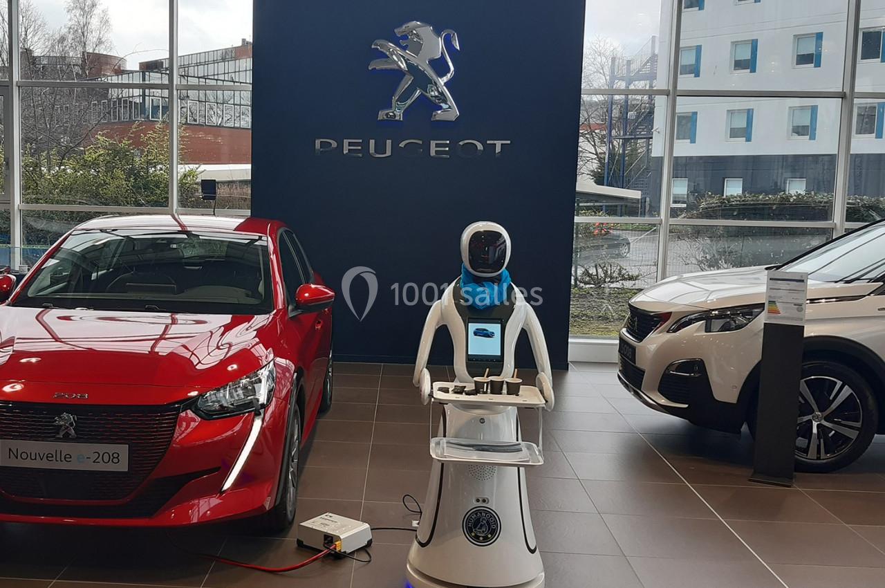 Un robot interactif exposé entre deux voitures Peugeot dans un showroom lumineux.