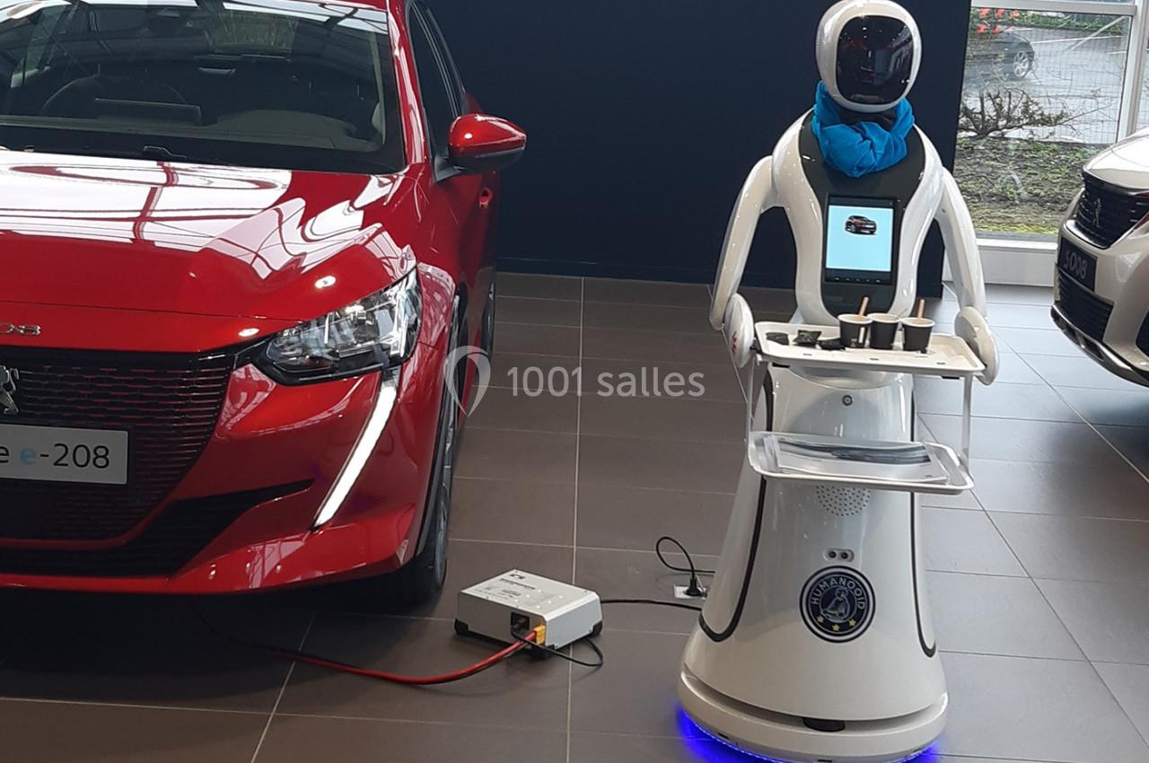 Un robot interactif à côté d'une voiture électrique rouge en charge dans un showroom automobile.