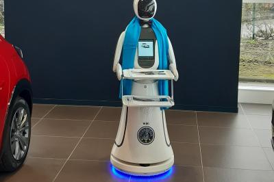 Robot humanoïde blanc équipé d'un écran et d'un plateau, présenté dans un environnement intérieur avec plantes et…