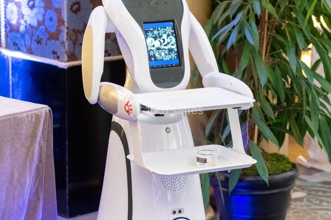 Robot humanoïde blanc équipé d'un écran et d'un plateau, présenté dans un environnement intérieur avec plantes et…