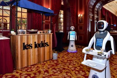 Robot humanoïde blanc équipé d'un écran et d'un plateau, présenté dans un environnement intérieur avec plantes et…