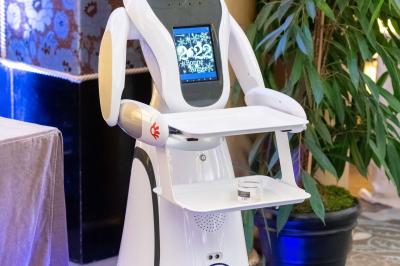 Robot humanoïde blanc équipé d'un écran et d'un plateau, présenté dans un environnement intérieur avec plantes et…