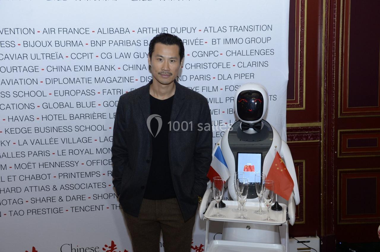 Un homme pose à côté d'un robot équipé de drapeaux français et chinois dans un cadre formel.