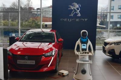 Robot humanoïde blanc équipé d'un écran et d'un plateau, présenté dans un environnement intérieur avec plantes et…