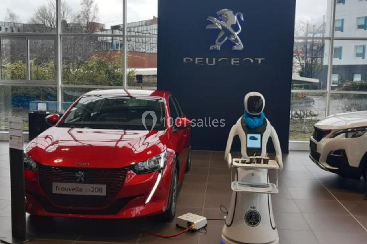 Trois voitures exposées dans un showroom Peugeot, avec un robot interactif au centre.