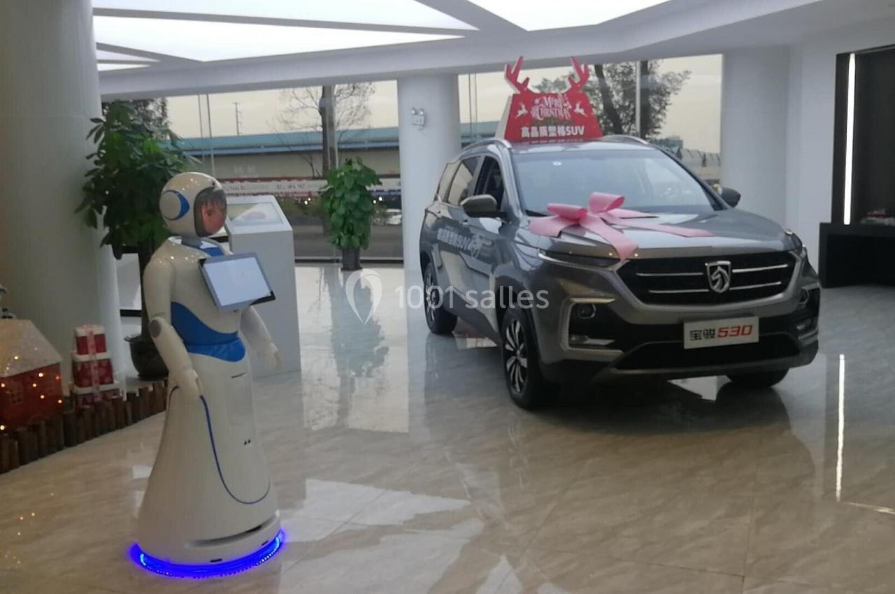 Un robot interactif devant un SUV gris décoré d'un nœud rose dans un showroom lumineux.