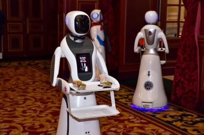 Robot humanoïde blanc équipé d'un écran et d'un plateau, présenté dans un environnement intérieur avec plantes et…