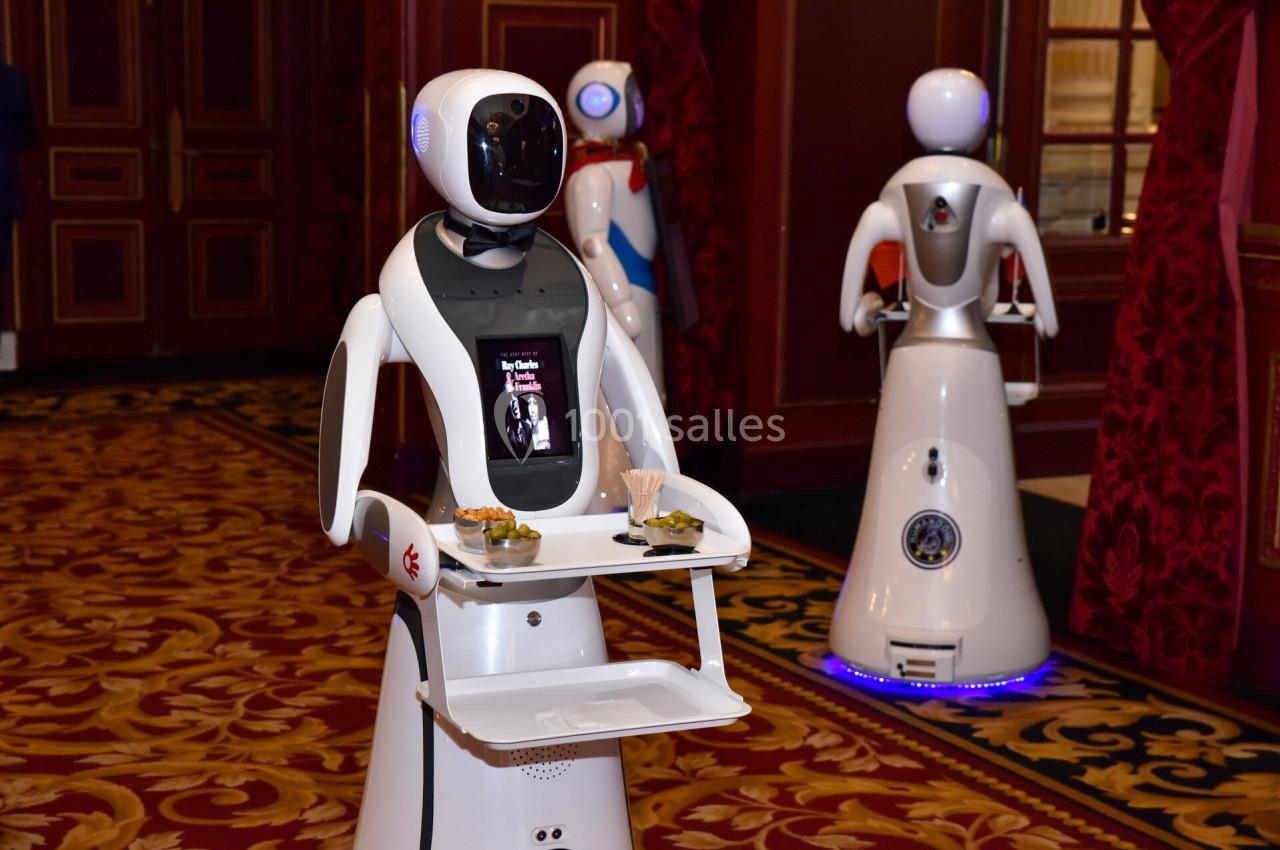 Des robots humanoïdes équipés de plateaux servent des amuse-bouches dans un intérieur élégant avec tapis rouge.