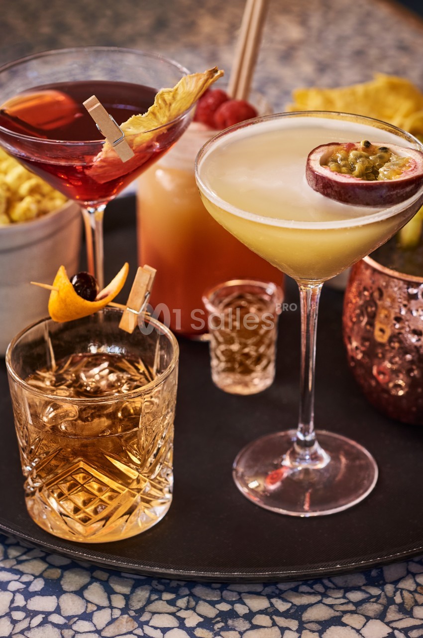 Plateau de cocktails variés avec garnitures, accompagné de popcorn et d'un verre en cuivre sur une table en mosaïque.