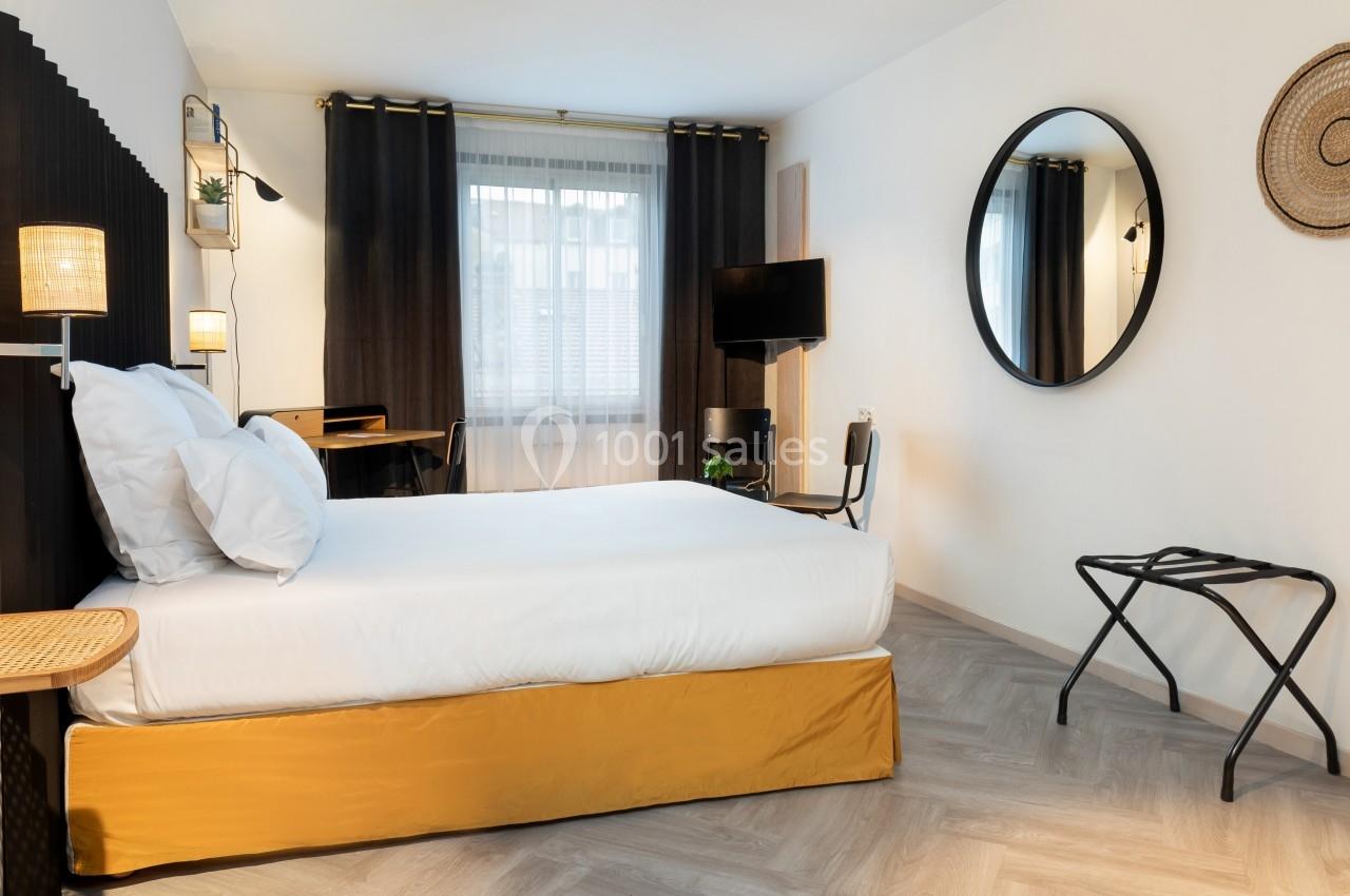 Chambre lumineuse avec lit double, bureau, télévision, miroir rond et décoration murale, parquet clair au sol.