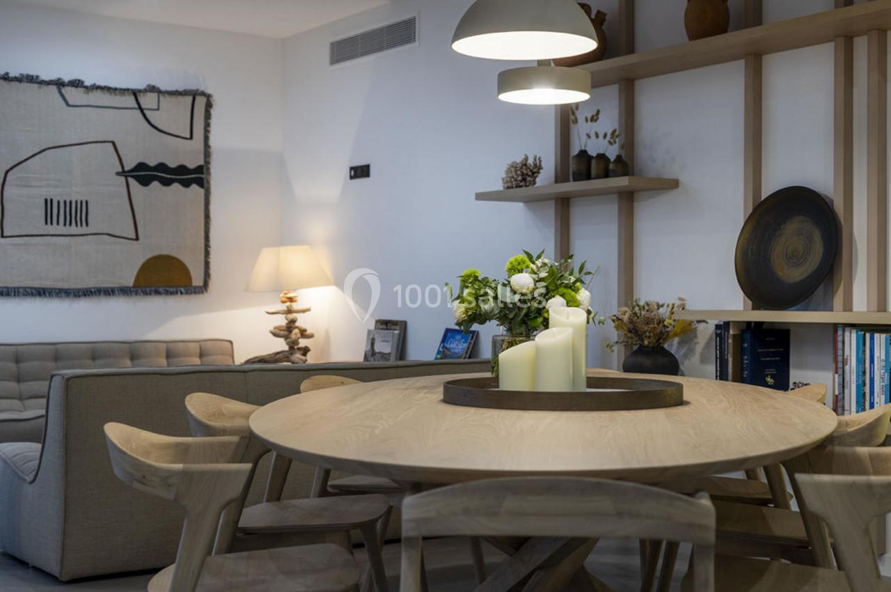 Salle à manger avec table ronde en bois, chaises assorties, étagères décorées et éclairage chaleureux.