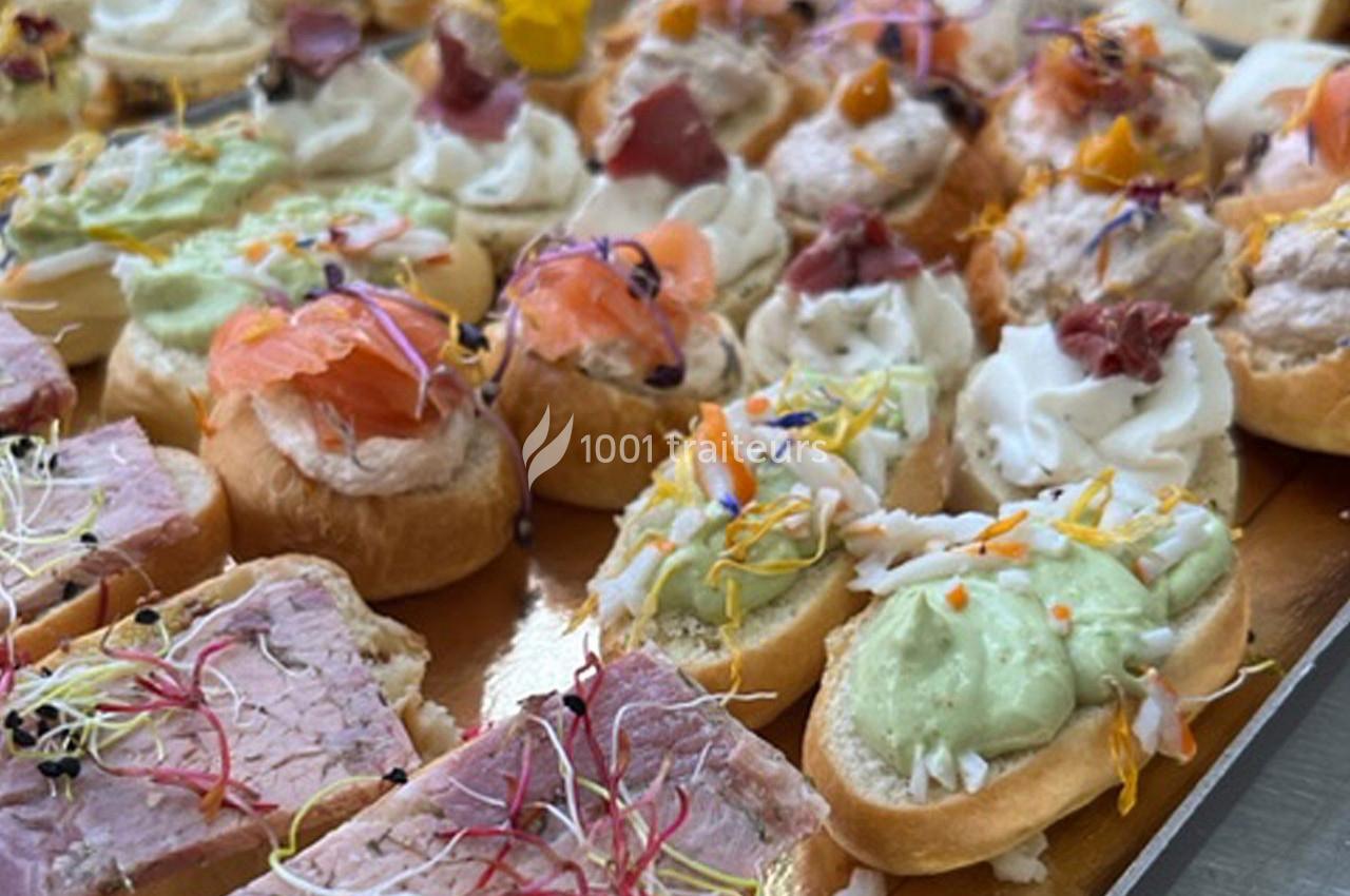 Plateau de canapés variés garnis de saumon, viande, mousse et décorés de fleurs comestibles et pousses colorées.