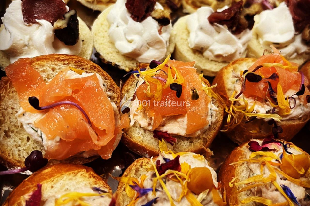 Assortiment de canapés garnis de saumon fumé, fromage frais et fleurs comestibles colorées.