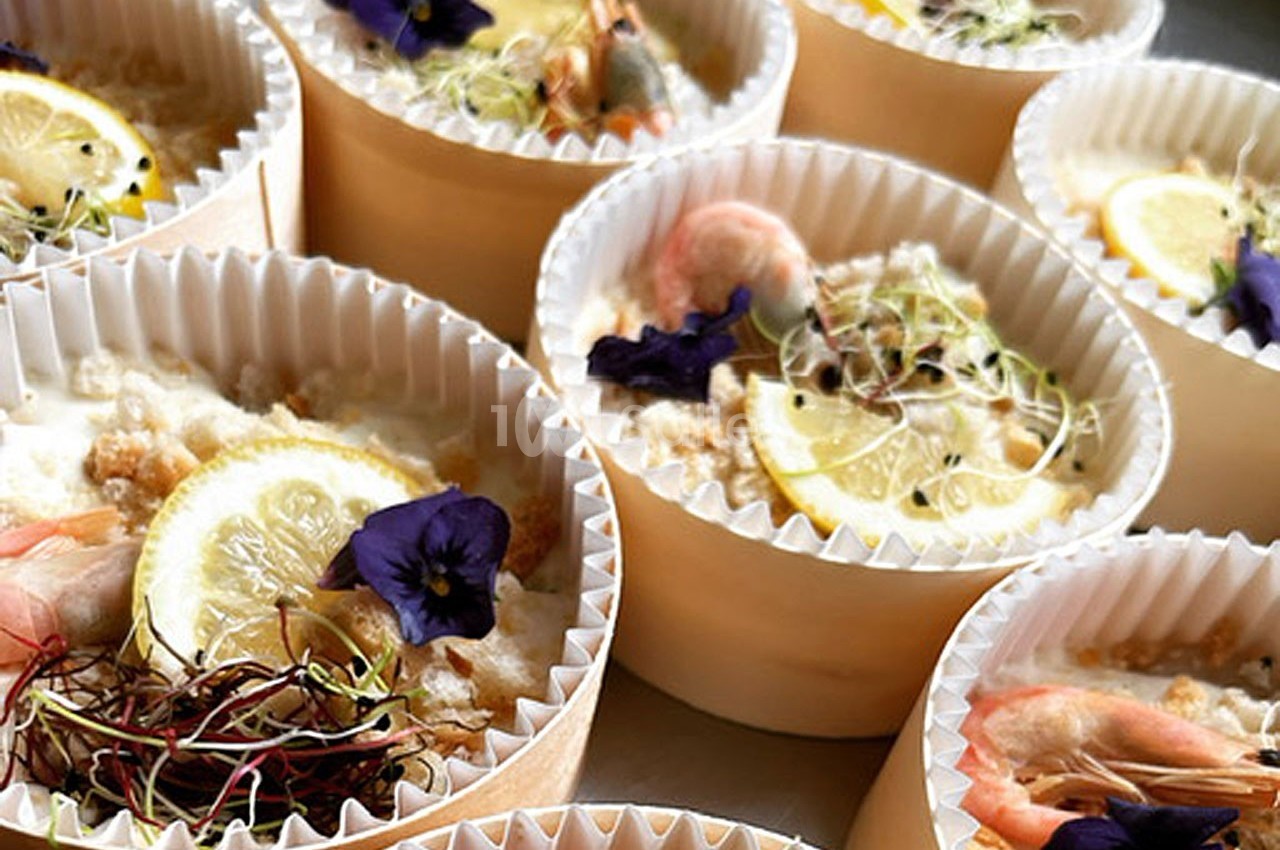 Coupes en carton contenant des plats garnis de crevettes, tranches de citron, pousses et fleurs comestibles.