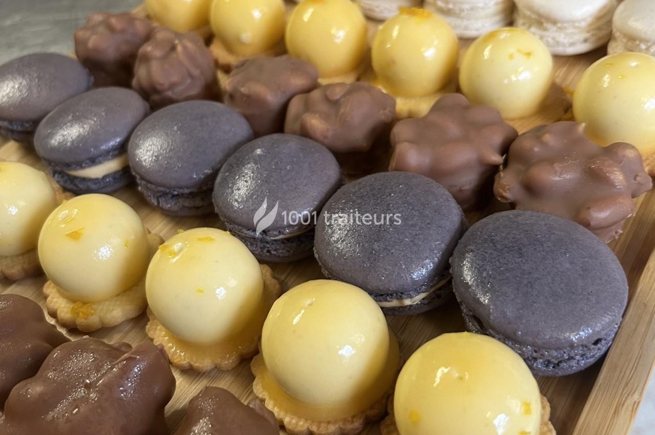 Assortiment de pâtisseries miniatures comprenant macarons violets, tartelettes jaunes et bouchées chocolatées.