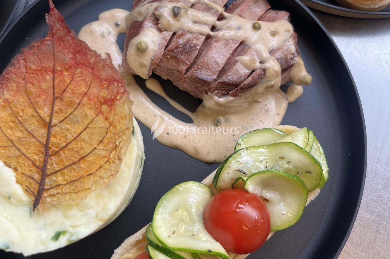 Assiette composée d'un steak nappé de sauce, purée décorée d'une feuille croustillante et garniture de légumes frais.