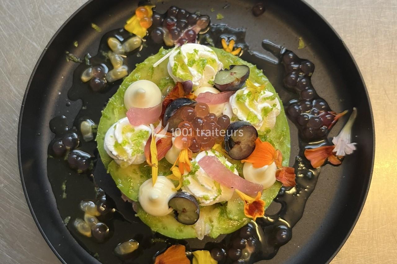 Assiette garnie de tranches d'avocat, crème, raisins, fleurs comestibles et perles de saveur sur une sauce.