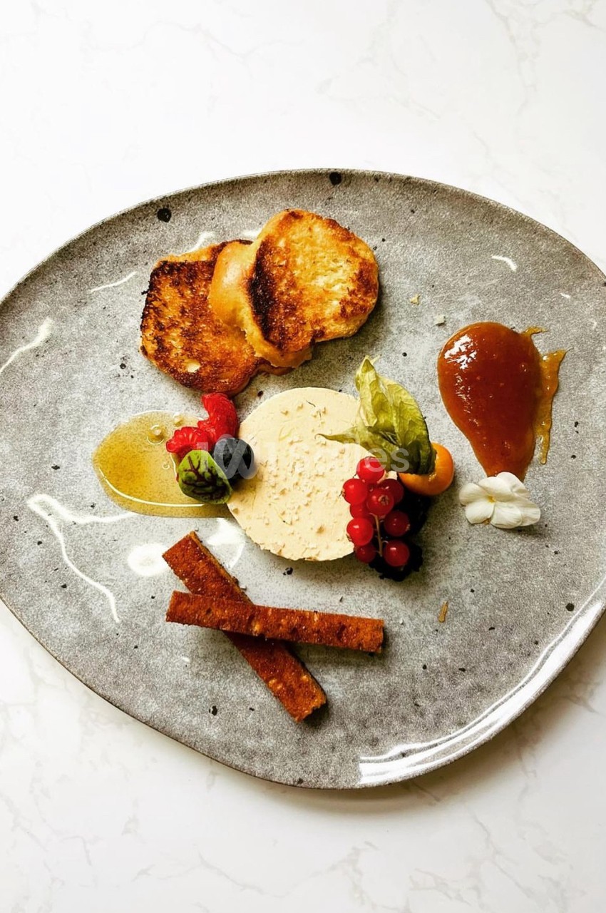 Assiette gastronomique avec foie gras, toasts, fruits rouges, chutney et garnitures sur une assiette grise.
