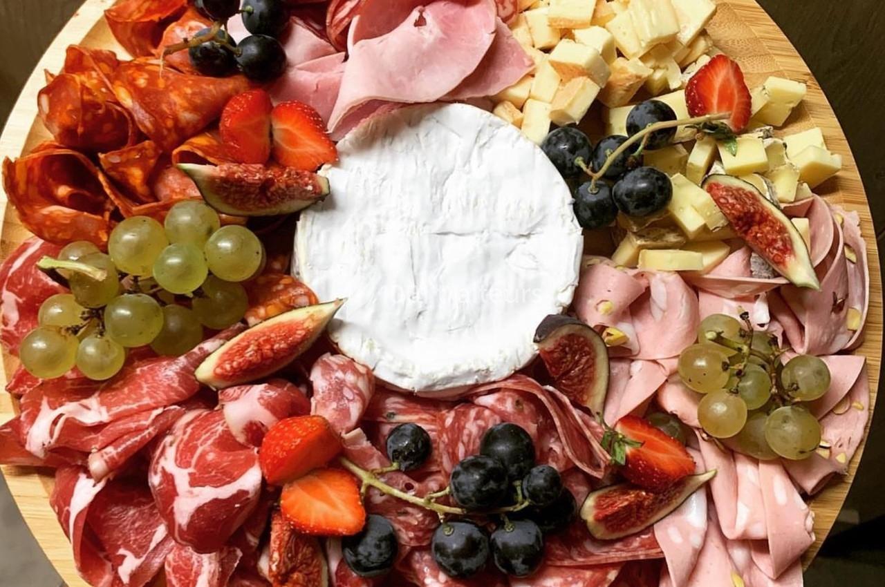 Plateau rond avec charcuteries variées, fromages, raisins, fraises et figues autour d’un fromage à pâte molle au centre.