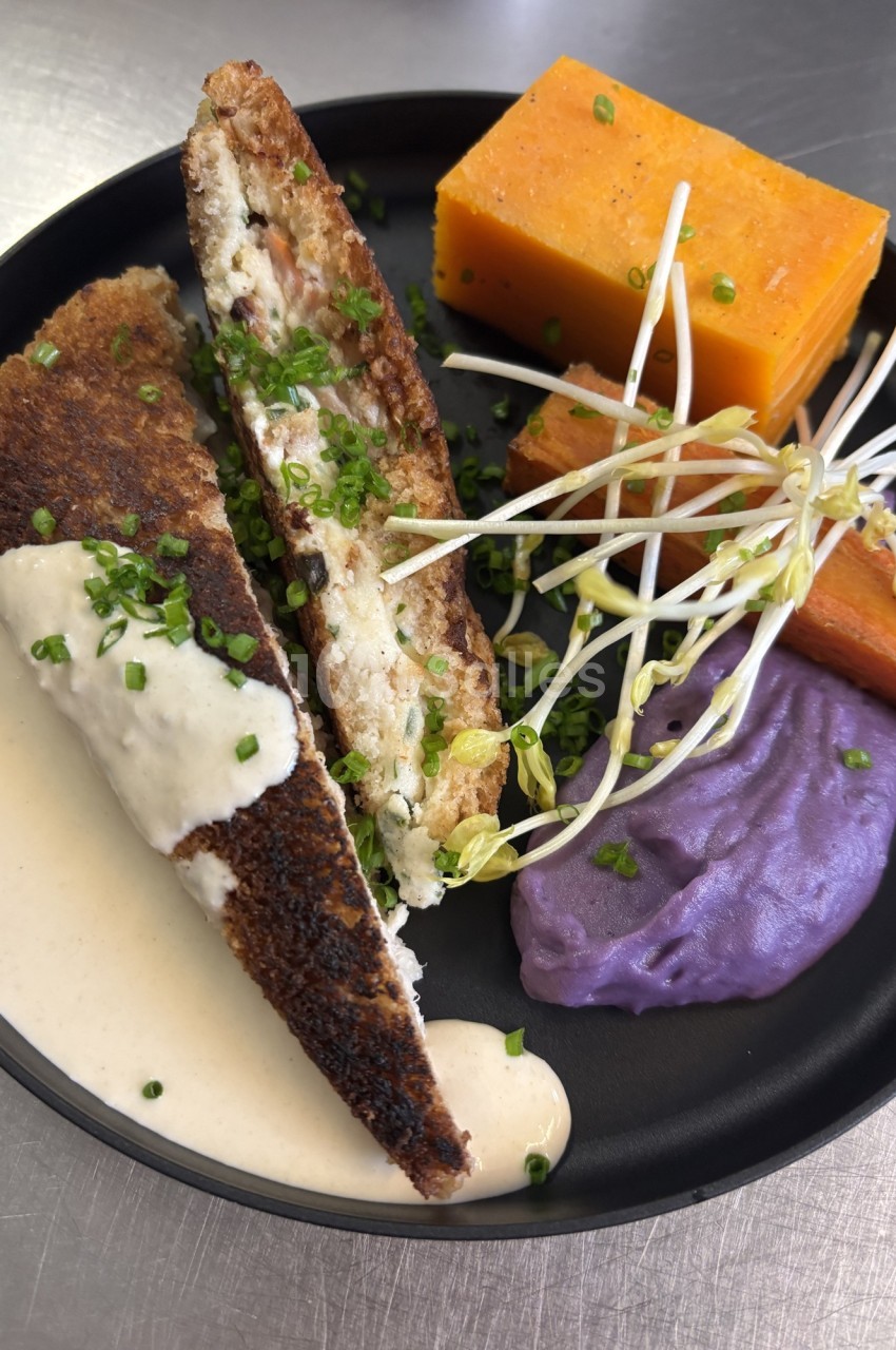 Assiette composée d'un croque revisité, purée violette, légumes racines et germes, nappée de sauce blanche.