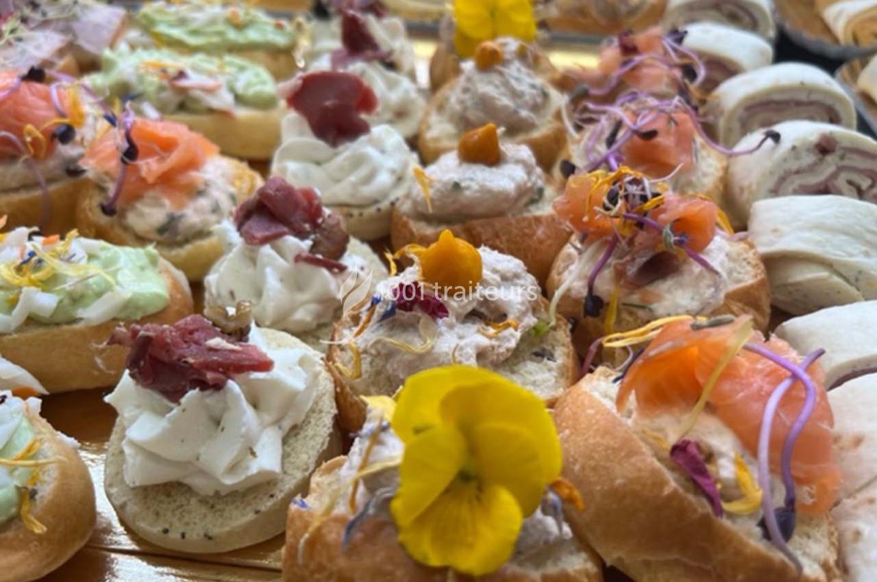 Assortiment de canapés variés garnis de saumon, fromage, crudités et fleurs comestibles.