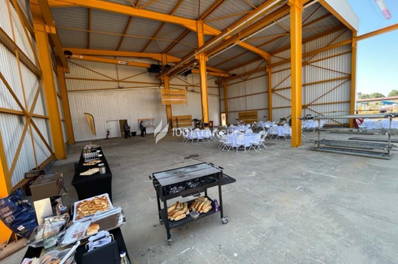 Salle industrielle avec tables rondes dressées pour un événement et buffet installé sur le côté.