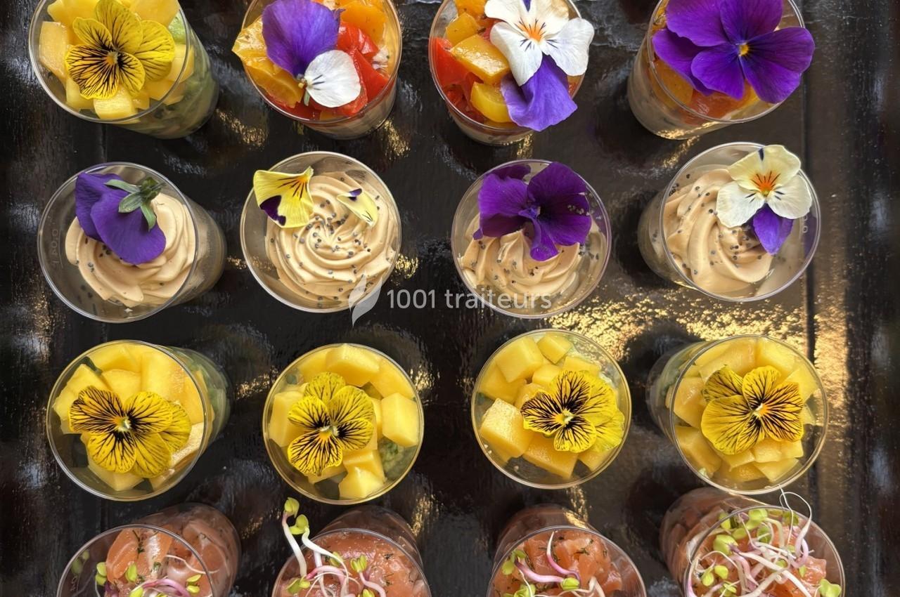 Plateau de verrines colorées garnies de fleurs comestibles, mousses et légumes, disposées en rangées.