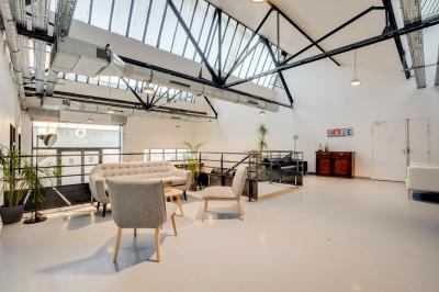 Intérieur d'un grand espace industriel lumineux avec sol clair, murs blancs, poutres métalliques et conduits apparents.