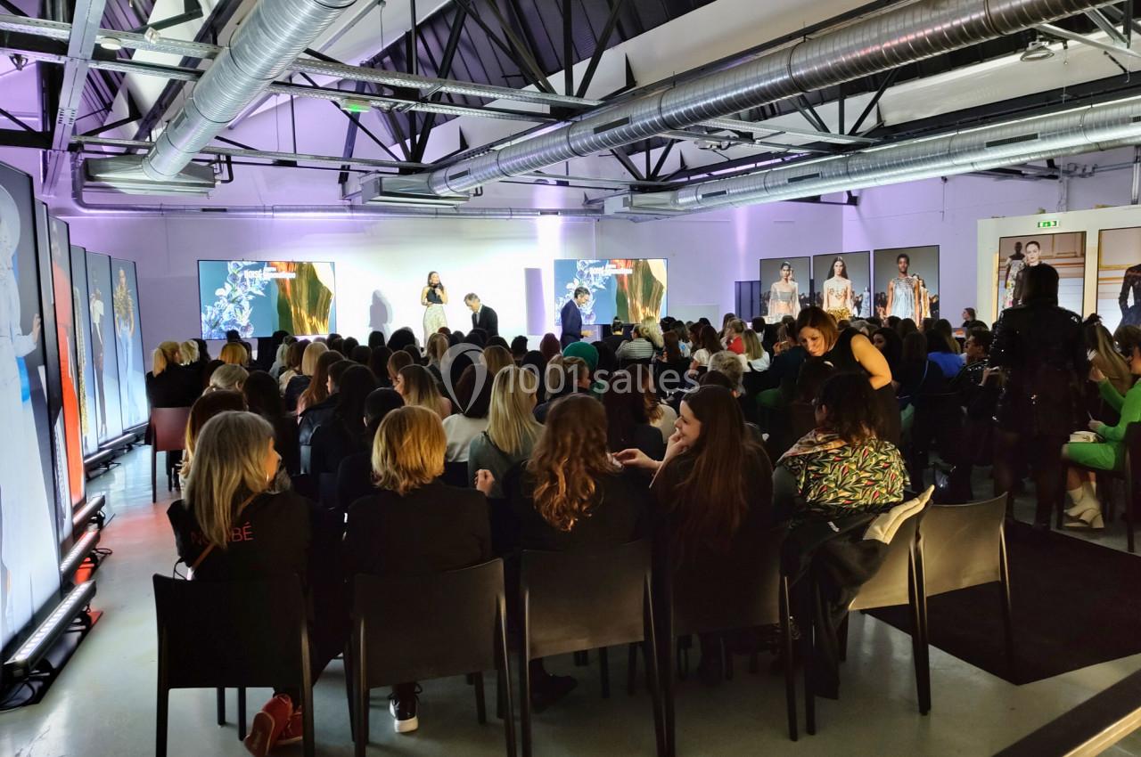Un groupe de personnes assises dans une salle moderne assistent à une présentation sur une scène éclairée.