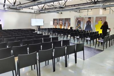 Intérieur d'un grand espace industriel lumineux avec sol clair, murs blancs, poutres métalliques et conduits apparents.