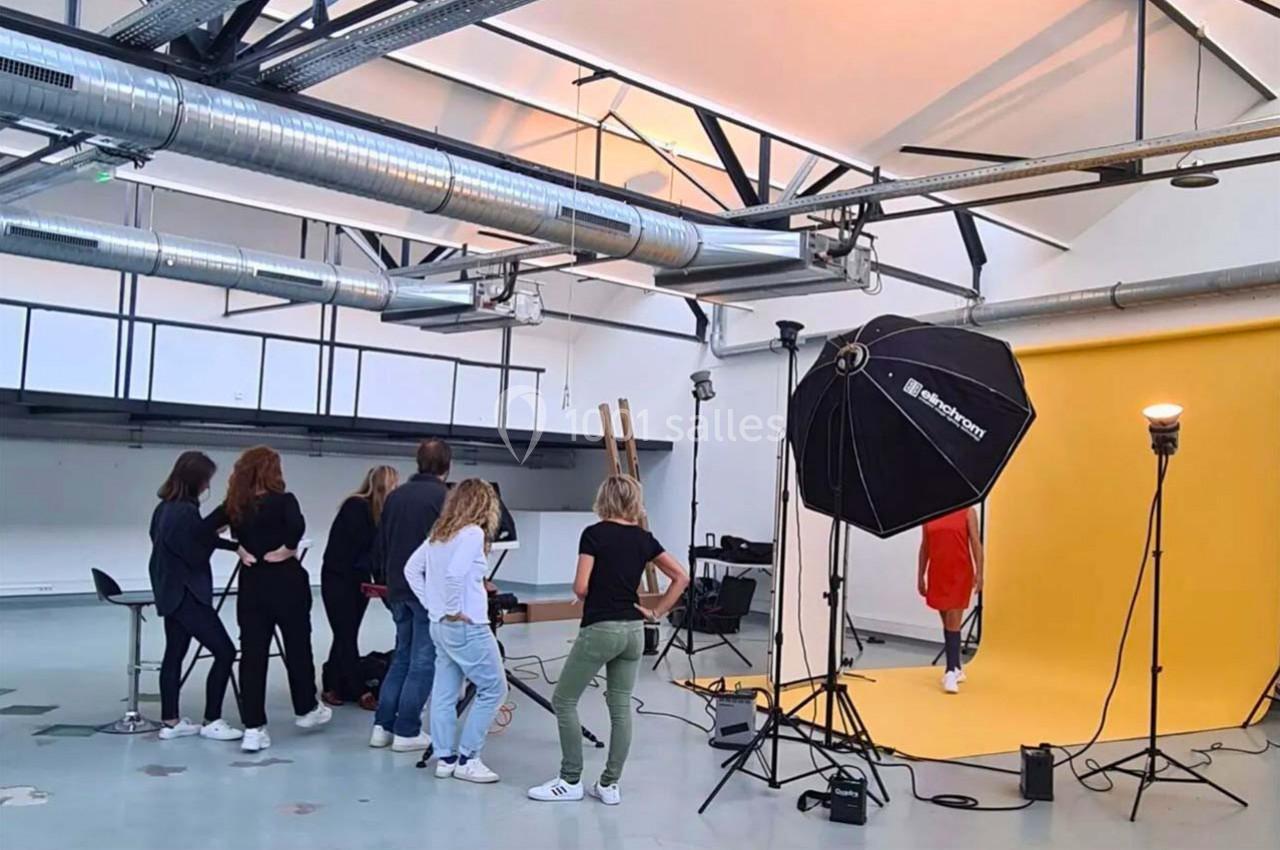 Des personnes observent une séance photo dans un studio avec un fond jaune et des équipements d'éclairage.