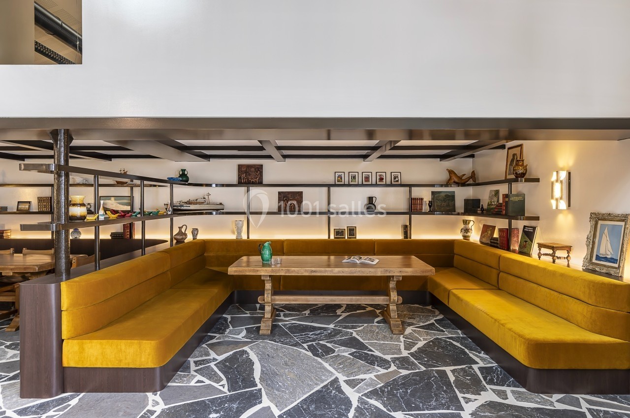 Banquette en velours jaune entourant une table en bois, avec des étagères décorées en arrière-plan.