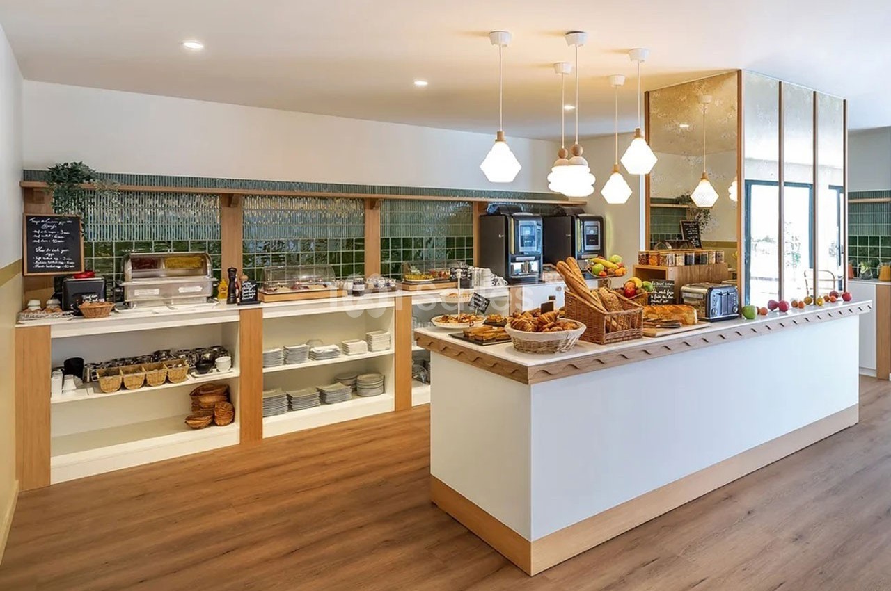 Buffet de petit-déjeuner avec viennoiseries, fruits, boissons et équipements dans une salle lumineuse au sol en bois.